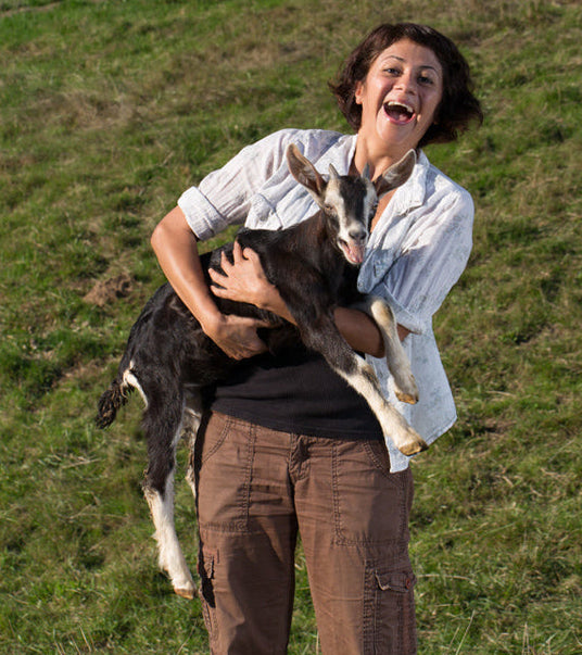Woman holding a goat in a grassy field