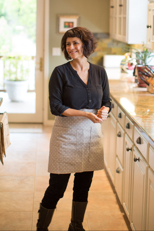 Woman standing in a modern kitchen with white cabinets and granite countertops.