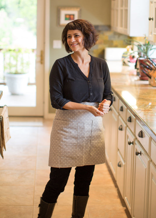 Woman standing in a modern kitchen with white cabinets and granite countertops.