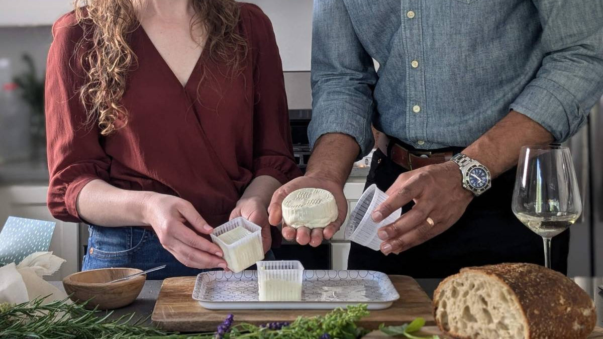 Two people in a kitchen preparing food, with a focus on bread and cheese.