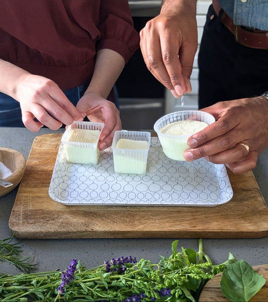 Two people preparing food on a kitchen counter with herbs and a cutting board.