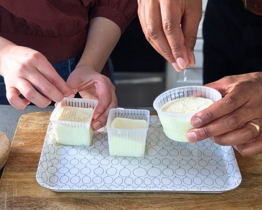 Two people preparing food on a kitchen counter with herbs and a cutting board.