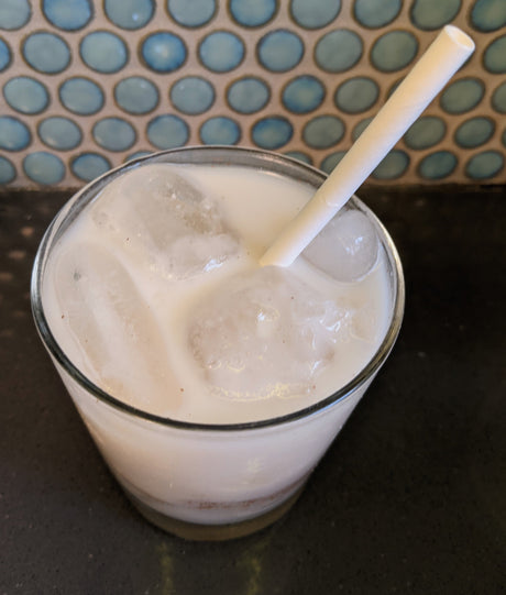 glass of whey horchat on ice with a straw and circle tile in the background