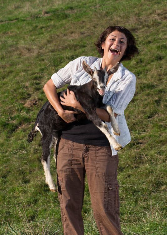 Woman holding a goat in a grassy field