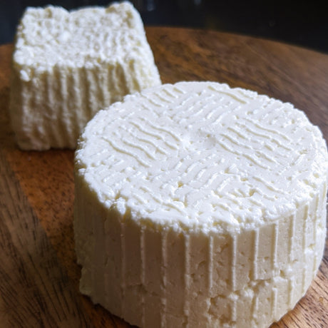 two wheels of fresh cheese on wood board 
