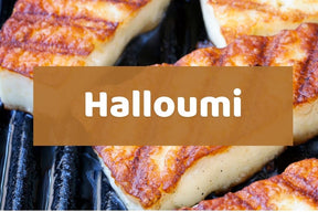 Grilled halloumi cheese slices with golden-brown charred marks on a dark grill, overlaid with a semi-transparent brown banner containing the white text 'Halloumi'.