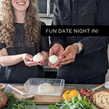 Two people holding their own homemade mozzarella balls with a text overlay 'FUN DATE NIGHT IN!' on a kitchen counter with food items.