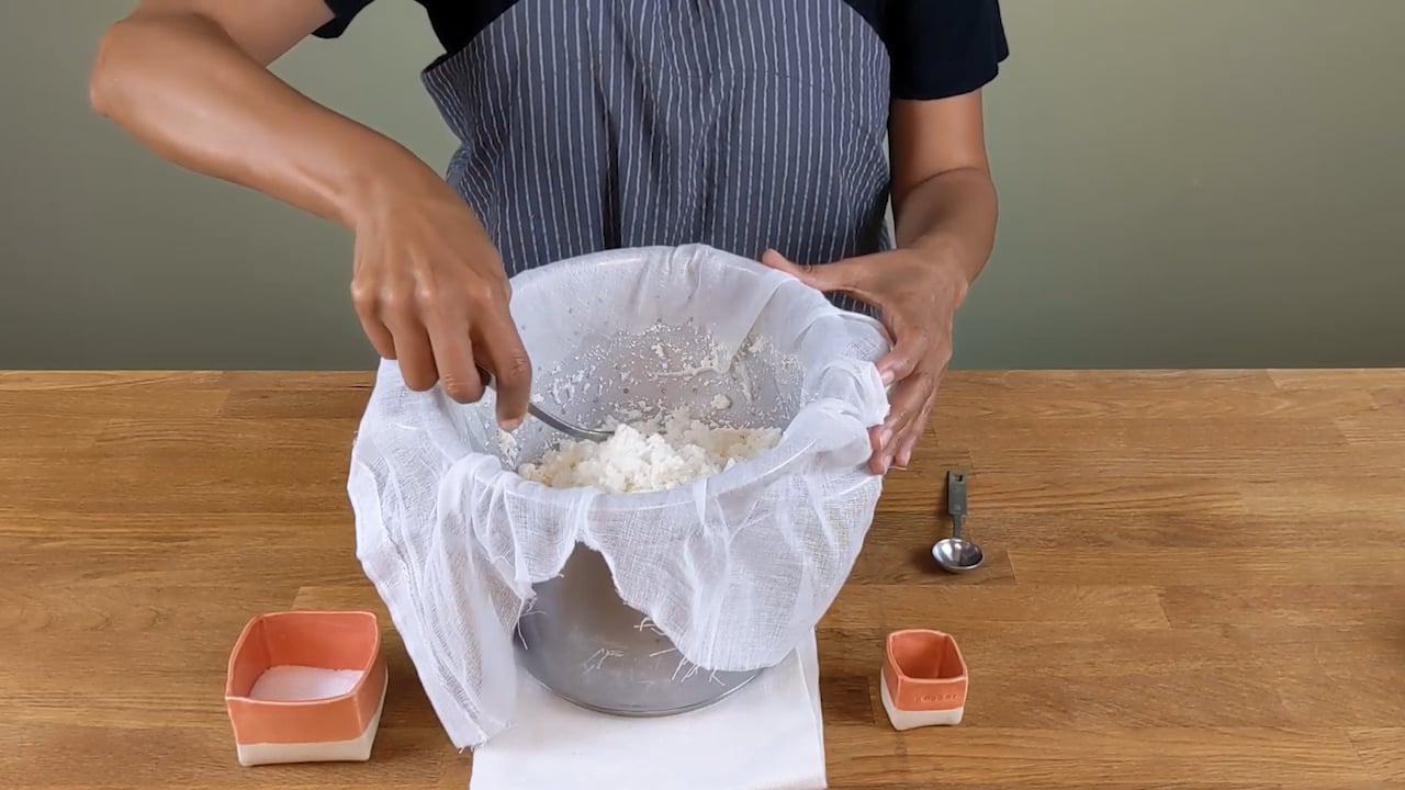 cheesemaker in apron salting fresh cheese in kitchen