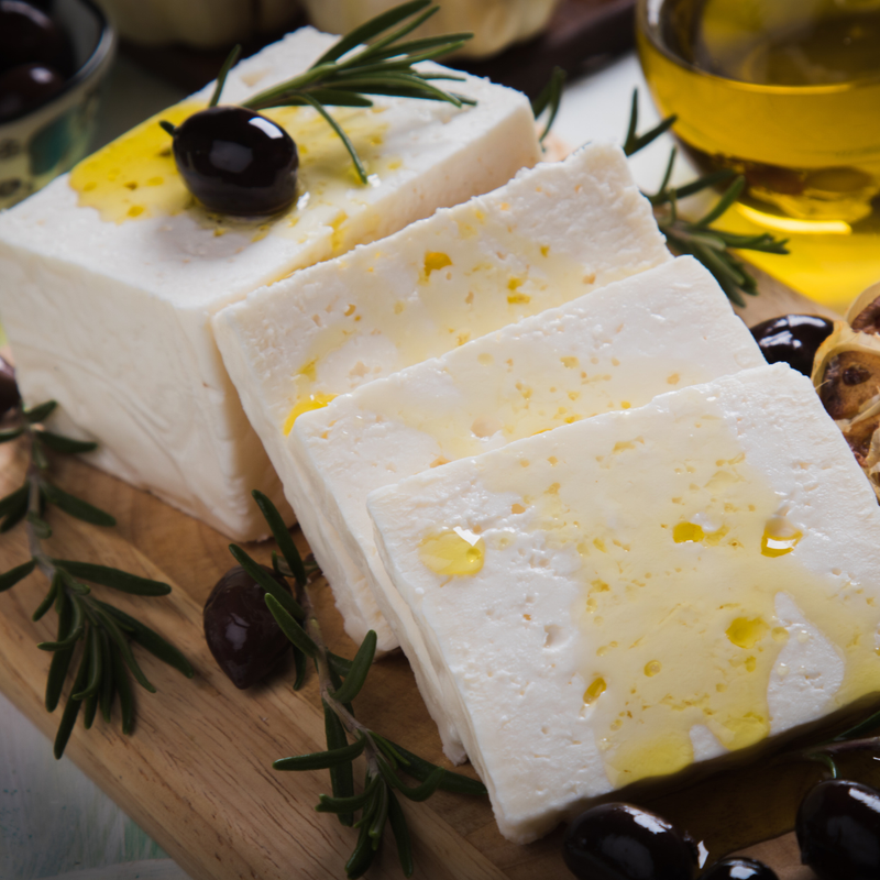 Slices of white cheese with olives and rosemary on a wooden board