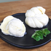 A sliced mozzarella ball oozing cream and a string cheese knot on a black plate with a sprig of green herbs on a wooden surface